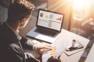 Businessman analyzes documents in his hands and graphs on his laptop