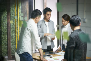 Four business-casual professionals standing in a room looking at documents