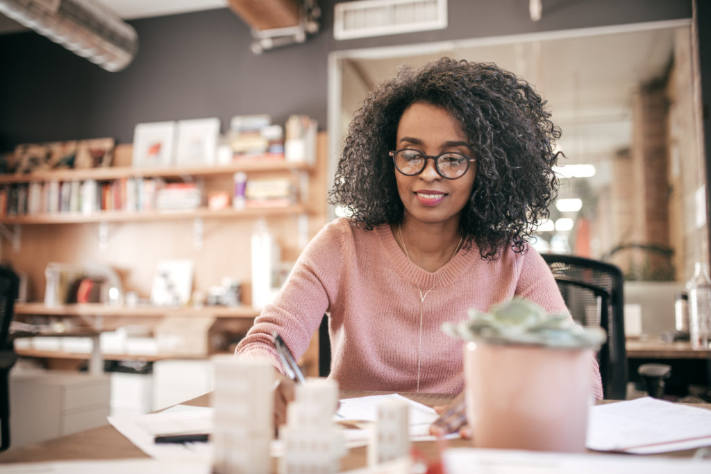 A Black woman in a pink sweater sits at a table calculating sums