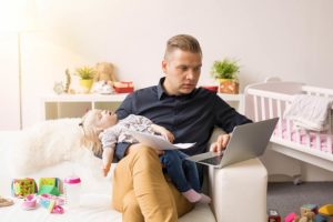 Busy father working on computer while holding sleeping baby