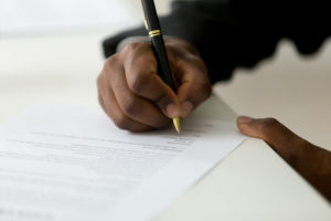 Close-up of a man holding a pen and signing financial documents