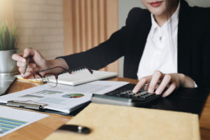 A woman wearing a black business suit types on a calculator and looks at financial documents