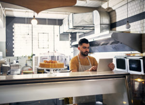 Picture of a young man using his tablet while working behind the counter in a coffee shop