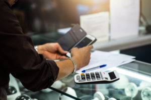 A woman's hands holding a cell phone and making calculations on a calculator