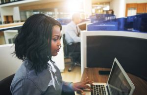 Young black woman with shoulder-length black hair types on a silver laptop in an office