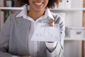 Feature image of a woman of color smiling and handing a check across a desk