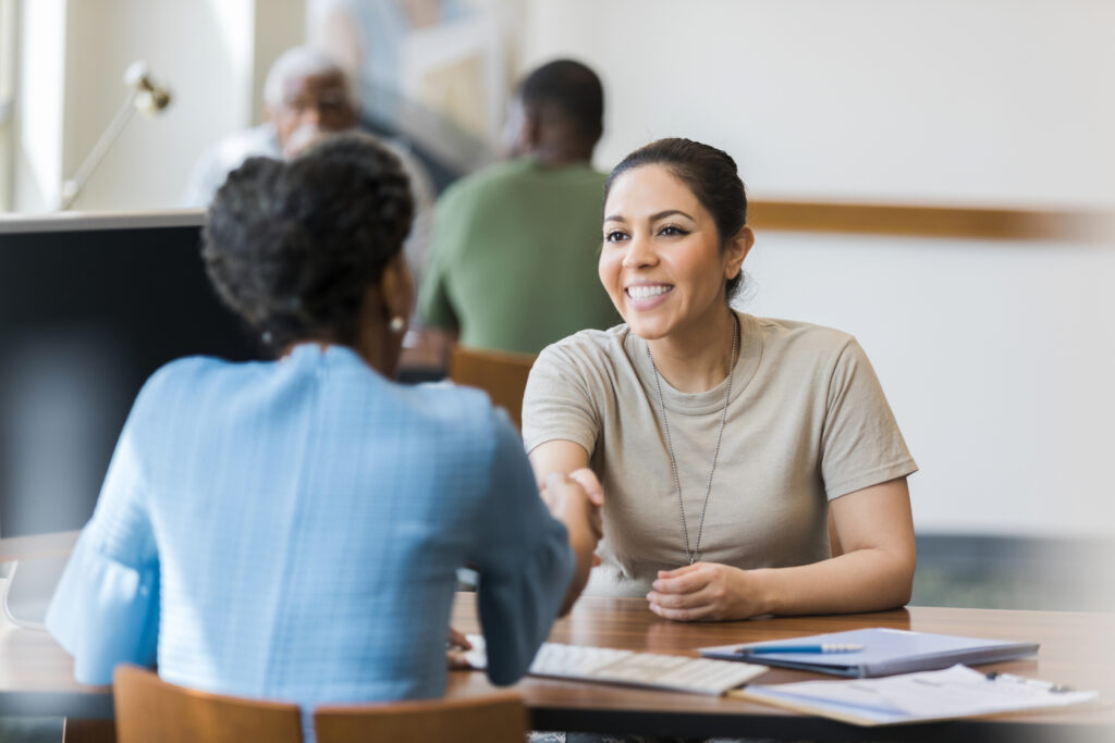 Two women sitting at a bank desk shaking hands