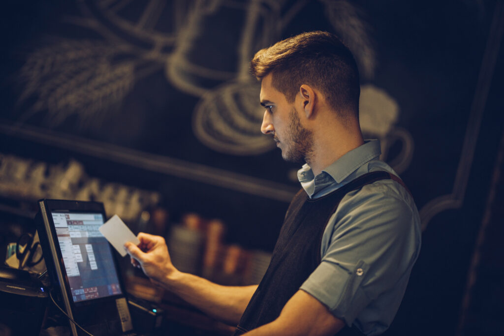 Young male waiter working at the point of sale in a bar.