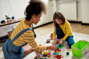 Feature image of a white girl playing with blocks with a black female caretaker