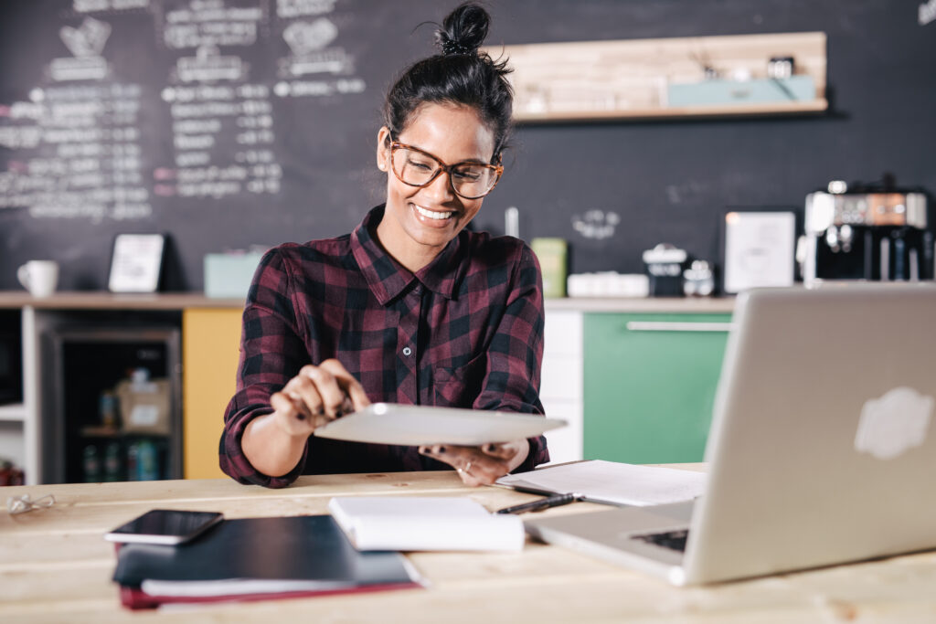 Featured image of a young woman sitting at a table in a cafe, smiling at a piece of paper