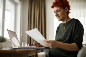 Feature image of a pregnant white woman with dyed red hair smiling at a piece of paper