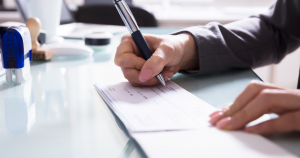 Close-up of a white woman's hands as she signs a cheque with a pen