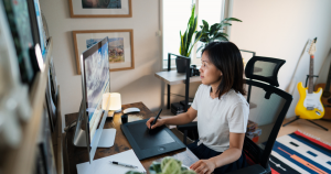 A young businesswoman draws on a tablet while sitting in front of a desktop computer