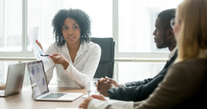 A Black businesswoman shows a financial form to a Black man and white woman