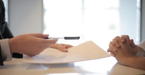 man handing a pen and paper over to another person to sign