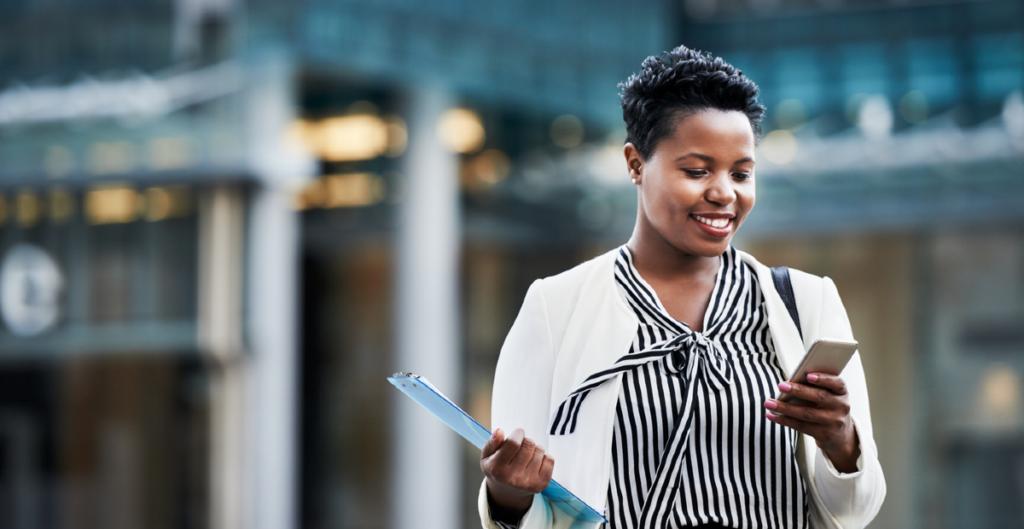 A Black woman wearing a black and white top smiles down at her mobile phone