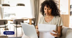 woman using computer and referencing sheet of paper