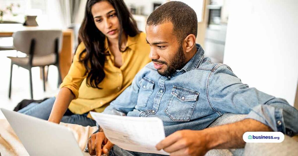 two-people-using-laptop-looking-at-paperwork